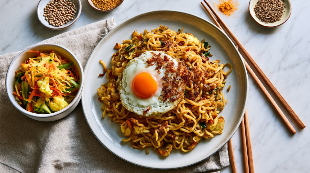 Kom met zelfgemaakte atjar tjampoer naast een bord bami goreng, een fris zoetzuur Indonesisch bijgerecht met kleurrijke groenten en kruiden.